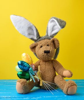 vintage cute brown teddy bear holding colorful Easter eggs, wearing a rabbit mask with long ears on his head, funny holiday card