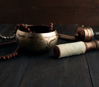 Tibetan singing copper bowl with a wooden clapper on a brown wooden table, objects for meditation and alternative medicine, close up