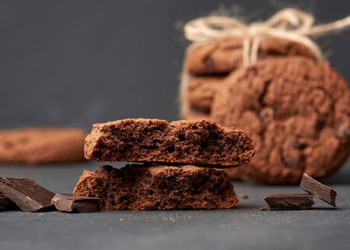stack of baked round chocolate chip cookies and pieces of chocolate on a black table, close up