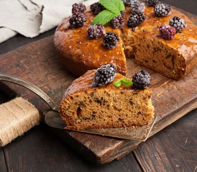 baked round sponge cake with nuts and topped with berries, wooden brown table, close up