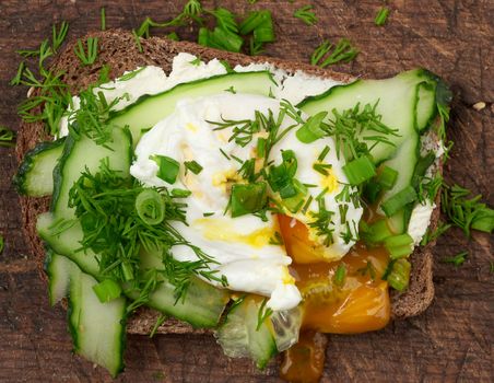 sandwich on toasted white slice of bread with poached eggs, green leaves of onion, morning breakfast on a brown wooden board, top view