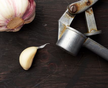 old metal garlic press and fresh young white garlic on a brown wooden table, top view