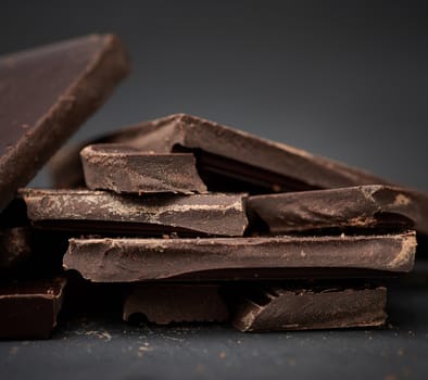 pieces of black chocolate on a black background, sweet dessert, close up