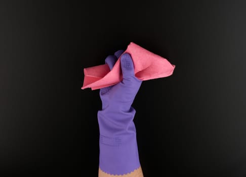 hand holds a pink rag sponge for cleaning, protective purple rubber glove is worn on the arm, black surface wash process