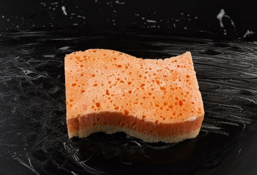 rectangular wet orange washcloth with white foam on a black background, top view
