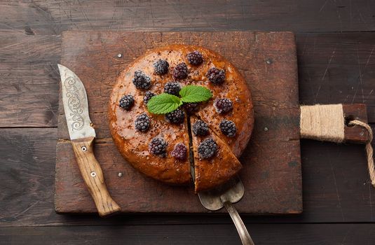 baked round biscuit cake with nuts and berries topped, wooden brown table, top view, sponge cake
