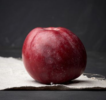 red ripe apple lies on a gray linen napkin, black background, close up