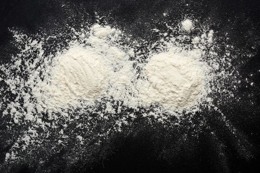 white wheat flour scattered on a black table, ingredient for the dough, top view