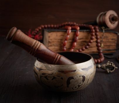 Tibetan singing copper bowl with a wooden clapper on a brown wooden table, objects for meditation and alternative medicine, close up