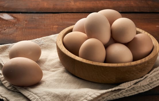 raw brown chicken eggs in a wooden plate on the table, top view