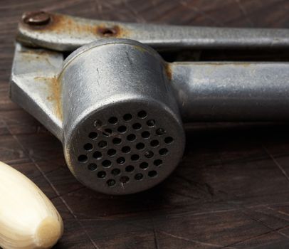 old metal garlic press and fresh young white garlic on a brown wooden table, close up