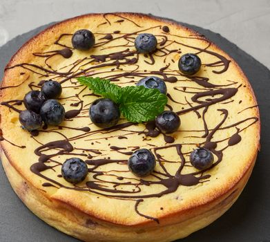 baked round cottage cheese casserole on a black plate, top view, tasty and healthy dessert