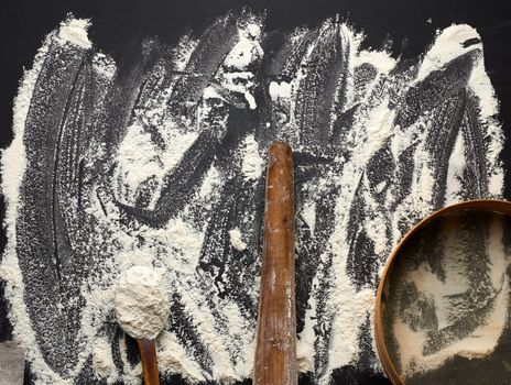 white wheat flour scattered on a black table and very old brown wooden rolling pin, round sieve, top view