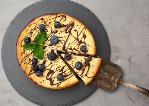 baked round cottage cheese casserole on a black plate, top view, tasty and healthy dessert