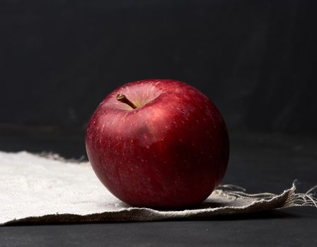 red ripe apple lies on a gray linen napkin, black background, close up