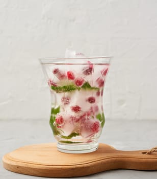 transparent glass with lemonade and pieces of ice, red berries on a white background, a refreshing summer drink