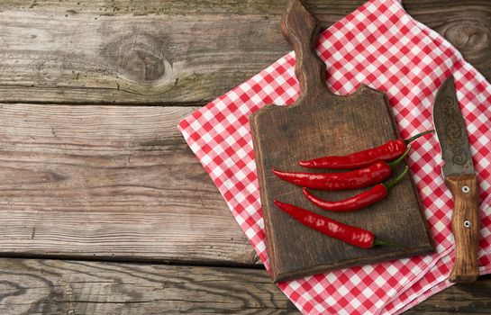 pods of red chili peppers on a brown cutting wooden board, gray table, top view, copy space