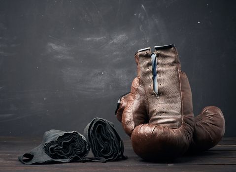 brown leather vintage boxing gloves and black elastic bandage for hands on a black background, sports equipment