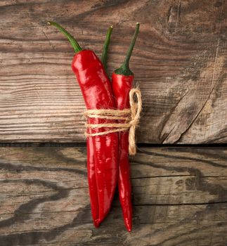 pods of red chili peppers tied with a brown rope on a gray wooden background, top view