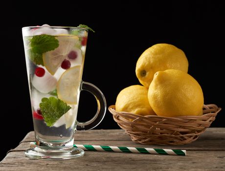 glass with lemonade and pieces of ice, red berries and paper tubes, a refreshing summer drink on a black background 