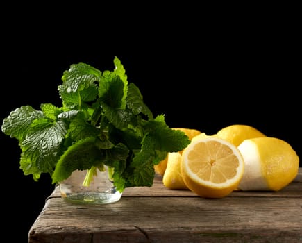 yellow ripe lemon and a bunch of fresh green mint on a wooden board, ingredients for lemonade, black background 