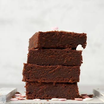 stack of square baked brownie chocolate cake slices on a white background, delicious dessert, close up