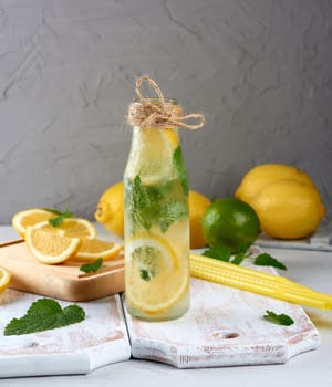 summer refreshing drink lemonade with lemons, mint leaves, lime in a glass bottle, next to the ingredients for making a cocktail