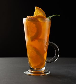 transparent large glass with a handle filled with lemonade with slices of orange, black background