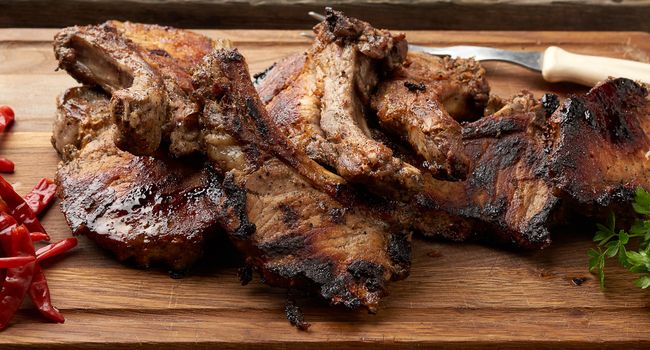 grilled pork steaks on the bone on a kitchen cutting board and red chili pepper, top view