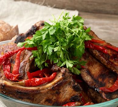 grilled pork steaks on the bone lie in a transparent glass plate on a wooden table, barbecue