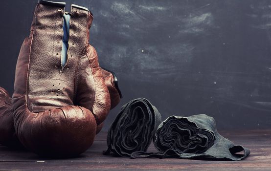 brown leather vintage boxing gloves and black elastic bandage for hands on a black background, sports equipment