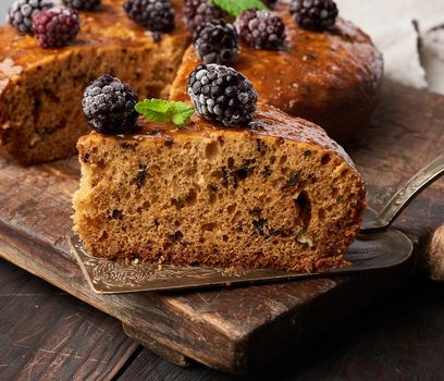 baked round sponge cake with nuts and topped with berries, wooden brown table, close up