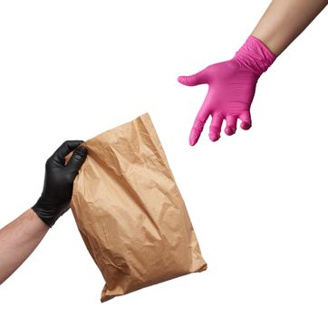 hand in a black latex glove holds a full brown package and a female hand in a pink glove reaches for an object, safe delivery of online orders, white background