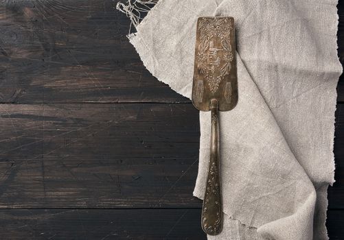 metal spatula for cakes on a brown wooden background with a gray linen towel, top view, place for an inscription