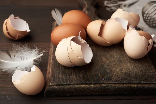 brown raw chicken eggs, shells, cutting board and hand-held whisk for protein on a wooden table, close up
