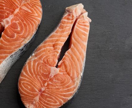 two raw salmon steaks on a black background, top view