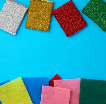 new multi-colored kitchen sponges for washing dishes on a blue background, flat lay, copy space
