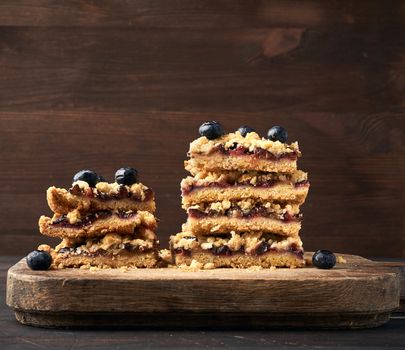 stack of square slices of baked crumble pie with blue plum on a wooden board, delicious dessert, close up