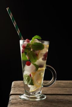 transparent glass with lemonade and pieces of ice, red berries and paper tubes, a refreshing summer drink on a black background