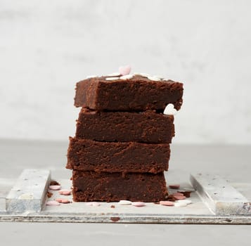 stack of square baked brownie chocolate cake slices on a white background, delicious dessert, close up