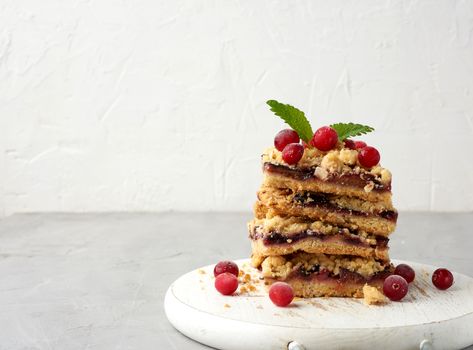 stack of square slices of baked crumble pie with blue plum on a white wooden board, delicious dessert, copy space