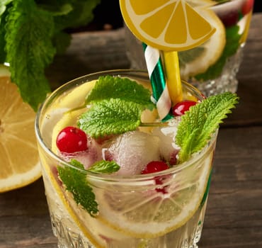 transparent glass with lemonade and pieces of ice, red berries, refreshing summer drink 