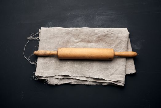 wooden rolling pin lie on a gray linen napkin, black table, top view, copy space