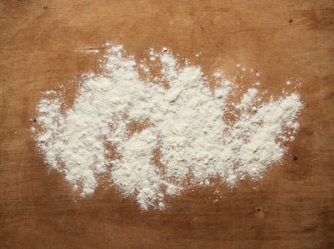 white wheat flour scattered on a brown wooden table, top view, kitchen backdrop