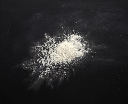 white wheat flour scattered on a black table, ingredient for the dough, top view