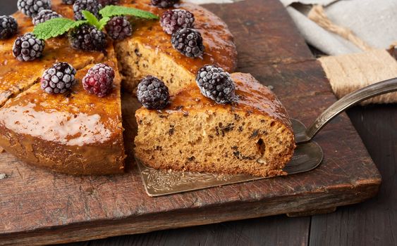 baked round sponge cake with nuts and topped with berries, wooden brown table, close up