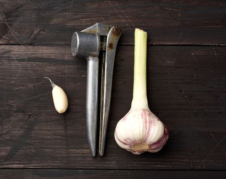 old metal garlic press and fresh young white garlic on a brown wooden table, top view