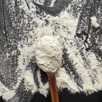 white wheat flour in a wooden brown spoon, black background, close up