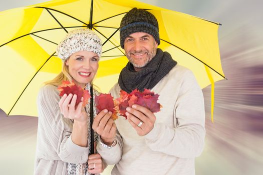 Couple in winter fashion showing autumn leaves under umbrella against room with large window looking on city