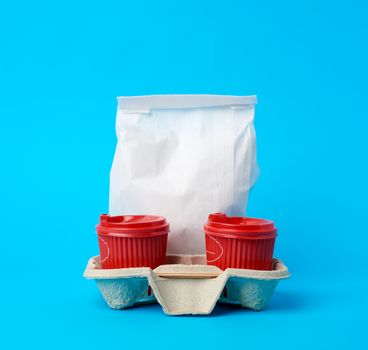 red disposable paper cups in the tray and a full white paper bag on a blue background, food delivery concept, order online